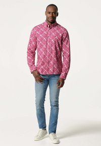 Lichtroze overhemd met een wit bloemenpatroon. Heeft een kraag, lange mouwen, en is gecombineerd met lichtblauwe jeans en witte sneakers.