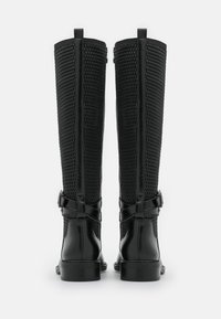 Bottes hautes noires jusqu'au genou avec une tige en maille texturée et des accents en cuir lisse, dotées d'un talon étroit et d'une bride ajustable.