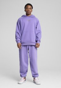 Lilla hættetrøje med lomme fortil og matchende sweatpants. Lavet af blødt materiale og med en diskret logo-detail på brystet og bukserne.