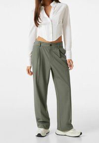 Camicia bianca leggera e cropped con chiusura a bottoni abbinata a pantaloni larghi color verde oliva a vita alta e sneakers bianche.