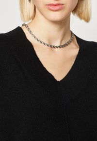 Svart stickad tröja med V-ringning, prydd med ett nära sittande silverfärgat tvisted kedja-halsband med en slät yta.