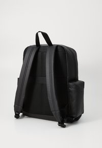 Black backpack with padded, adjustable straps, mesh back panel, and a side pocket. Made of durable, smooth material. Simple, functional design.
