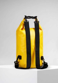 Sac à dos étanche jaune avec un design à rabat, des sangles en toile noires, du matériel en métal et un extérieur texturé.