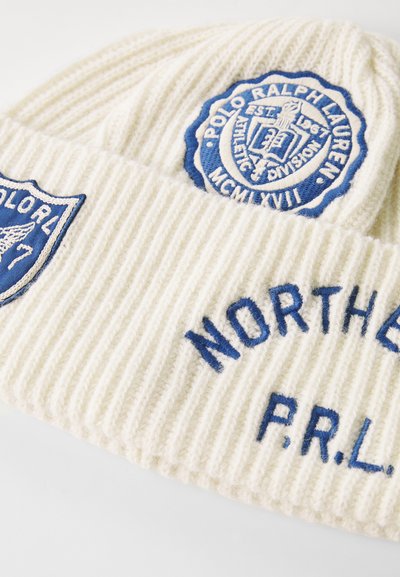 Biela rebrovaná pletená čiapka so získanými modrými výšivkami, vrátane kruhového loga a textu "NORTHERN P.R.L." s jemnými detailmi.