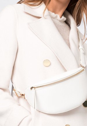 Biała skórzana torba na pasek z złotym suwakiem i elementami metalowymi, o zaokrąglonym kształcie. Ustawiona na tle jasnego płaszcza z złotymi akcentami.
