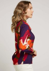 Chemise à manches longues colorée avec des motifs abstraits en rouge, rose et vert sur un fond violet ; tissu texturé ; design à col.