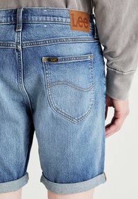 Jasnoniebieskie szorty dżinsowe z podwiniętymi mankietami, z skórzaną metką z napisem "Lee", przeszyciami na tylnej kieszeni oraz z wyblakłą fakturą.