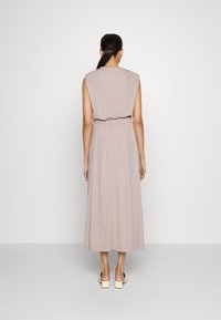 Maxi sukienka w miękkim beżowym materiale, bez rękawów, z wcięciem w talii i luźnym krojem, charakteryzująca się gładką fakturą i minimalnymi detalami.