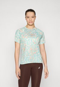 Camiseta atlética de color azul claro con patrones abstractos en coral, de mangas cortas y cuello redondo, combinada con leggings marrones que presentan un logo.