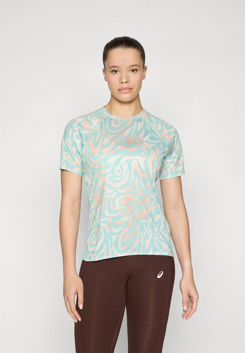 Camiseta atlética de color azul claro con patrones abstractos en coral, de mangas cortas y cuello redondo, combinada con leggings marrones que presentan un logo.
