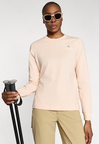 Lichtroze langemouwshirt met een ronde hals en een klein blauw logo, gecombineerd met beige broek en zwarte wandelschoenen.