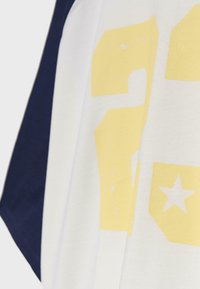 Gros plan sur un tissu blanc et bleu foncé avec des chiffres jaunes en bloc délavés et un graphisme d'étoile sur la section blanche.