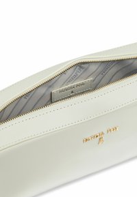 Pochette in pelle color crema con hardware dorato, esterno liscio e interno foderato con etichetta del logo. Chiusura con zip nella parte superiore.