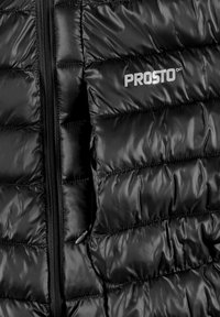Czarna puchowa kurtka z błyszczącym wykończeniem, posiadająca pikowane sekcje, zapięcie na zamek z przodu oraz widoczne logo na wysokości klatki piersiowej.