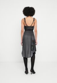 Čierne saténové šaty s hlbokým výstrihom na chrbte, tenkými ramienkami a asymetrickým lemom. Súčasťou je bočná kapsa s grafickými potlačami.