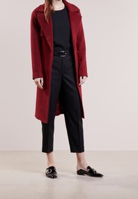 Röd ullblandad kappa med snedskuren krage, enkel knappstängning och sidofickor, i kombination med svarta höga byxor och svarta mules.