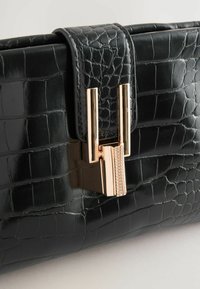 Čierna kožená clutch kabelka s embosovaním v tvare krokodíla a zlatým zapínaním, ktoré má textúrovaný akcent a hladký povrch.