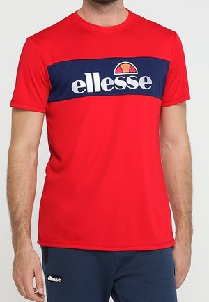 Mężczyzna ubrany w czerwony krótki rękaw z granatowym paskiem i białym logo "ellesse" na wysokości klatki piersiowej.