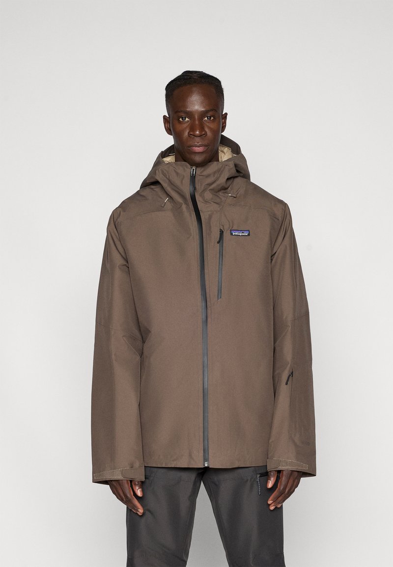 Chaqueta impermeable marrón con capucha, cremallera frontal y bolsillos laterales. Diseñada con una textura suave y un corte amplio para mayor comodidad.