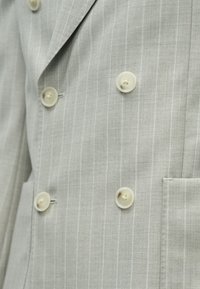 Lysegrå dobbeltradet blazer med nålestriber, fire cremefarvede knapper og en synlig forlomma.