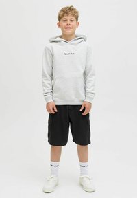 Svijetlo siva dukserica s prednjim džepom i crnim logom, u kombinaciji s crnim cargo šortsevima. Bijele čarape i bijeli tenisice zaokružuju ovaj look.