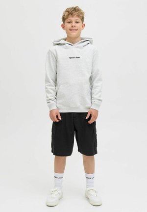 Lichtgrijze hoodie met een voorvak en zwart logo, gecombineerd met zwarte cargoshorts. Witte sokken en witte sneakers maken de outfit compleet.