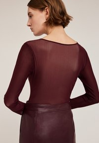 Bordeaux lange mouw top met een doorschijnende textuur en een ronde hals aan de achterkant, gecombineerd met een bijpassende strakke leren rok.
