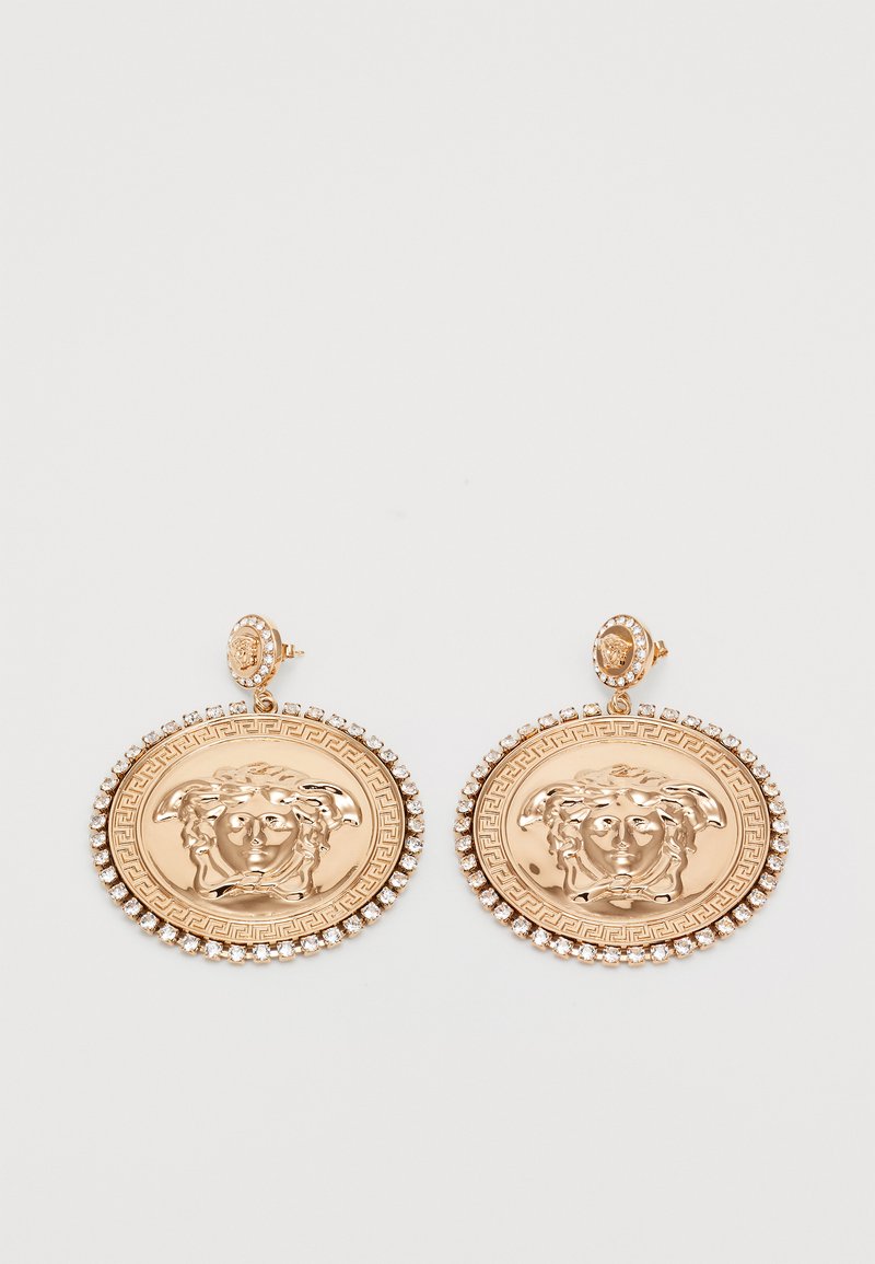 Χρυσές σκ earrings που απεικονίζουν κεφάλι Μεδούσας με κρυστάλλινη περίμετρο και σχέδιο ελληνικού κλειδιού σε λευκό φόντο.
