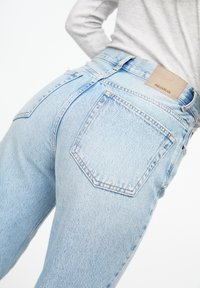 Jeans din denim bleu deschis cu talie înaltă, având un design clasic cu cinci buzunare și o etichetă din piele cu inscripția "PULL&BEAR" pe spate.