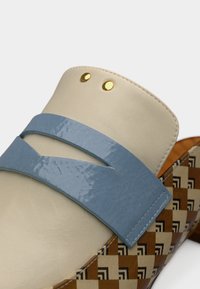 Chaussure à enfiler en cuir avec une tige beige, une bride bleue brillante, des accents métalliques dorés et une base à motifs marron et crème.