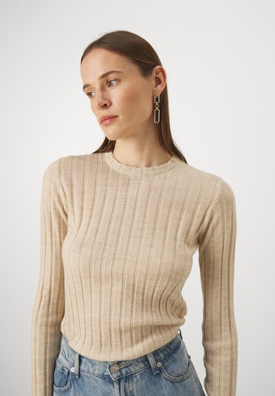 Haut à manches longues en tricot côtelé beige avec un col rond, associé à un jean taille haute bleu clair. Remarquable pour son tissu texturé et sa coupe ajustée.