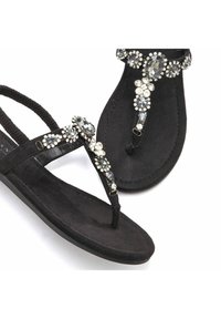 Sandales en suede noir avec un accent décoratif en cristal et strass sur le dessus, dotées d'une semelle plate et d'un design de bride en tongs.