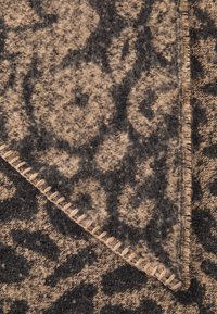 Coperta di lana con un motivo floreale marrone e nero, con una superficie texturizzata e cuciture intrecciate lungo il bordo.