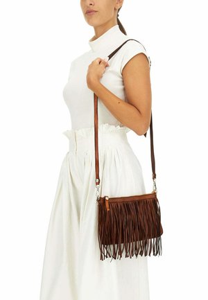 Borsa a tracolla in pelle marrone con dettagli in frange, chiusura con zip e tracolla regolabile. Indossata sopra una maglietta e una gonna bianche.