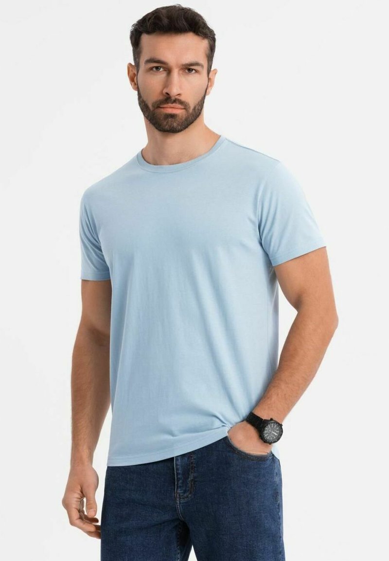 Camiseta de manga corta azul claro, hecha de algodón suave, con cuello redondo y corte recto, combinada con unos pantalones vaqueros oscuros.