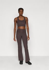 Smeđi sportski crop top i raskošne tajice od rastezljivog materijala, u paru s crnim sportskim tenisicama. Jednostavan dizajn, glatka tekstura.