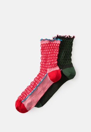 Chaussettes colorées présentant un motif en maille texturée rose et rouge d'un côté et noir uni avec des accents verts de l'autre. Bords festonnés.