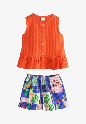 Haut sans manches orange texturé avec boutons à l'avant et ourlet à volants, associé à un short patchwork floral coloré avec bordure à volants.