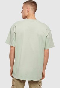Light green oversized cotton t-shirt with short sleeves, round neck, and clean stitching, displayed from the back.