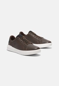 Bruna lädersneakers med vita sulor och bruna snören, visade sida vid sida på en enkel vit bakgrund.