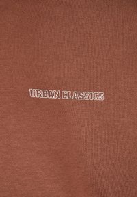 Pruun puuvillane dressipluus, millel on ees bold kirjas "URBAN CLASSICS" valge logo. Sujuv tekstuur ja igapäevane disain.