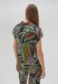 Short-sleeved shirt in black with colorful leaf patterns in green, pink, and orange. Smooth fabric with a relaxed fit and collar detailing.