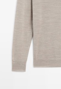 Tissu de pull beige clair avec une texture douce, comprenant une manche longue et un détail de poignet côtelé. Le matériau semble lisse et à maille fine.