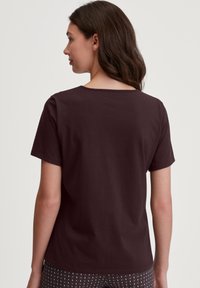 Bordeaux katoenen t-shirt met korte mouwen en een ronde hals. Soepele textuur, losse pasvorm, zichtbare stiksels aan de zoom.
