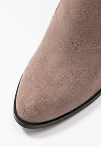 Botín de ante topo con punta afilada, textura suave y suela de goma negra. El diseño no presenta herrajes ni patrones visibles.