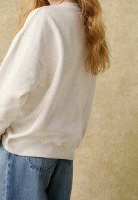 Sweat-shirt gris clair à coupe décontractée, texture douce, col rond et épaules tombantes, associé à un jean en denim bleu.