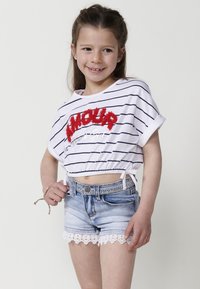 Top corto de algodón a rayas con la palabra "Amour" en bordado rojo texturizado, combinado con pantalones cortos de mezclilla con un ribete de encaje. Ambos en colores claros.