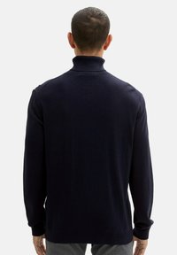 Granatowy sweter z golfem wykonany z teksturowanej dzianiny, z długimi rękawami, wysokim kołnierzem oraz luźnym krojem z prążkowanymi mankietami i dołem.