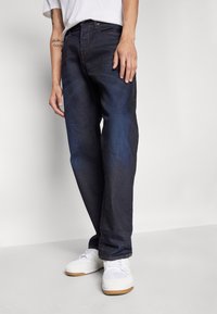 Mørkeblå denim jeans med lige pasform, udstyret med kontrastsyede orange stikninger og fem lommer, parret med hvide sneakers.