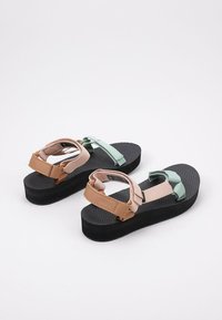 Sandalias multicolores con una suela negra texturizada, tiras en rosa, verde y marrón, con cierres ajustables para un ajuste seguro.
